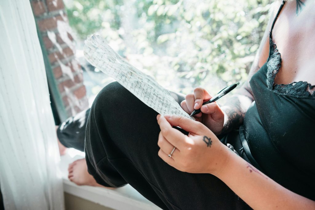 A person in black spaghetti strap sitting on a windowsill while writing on a paper